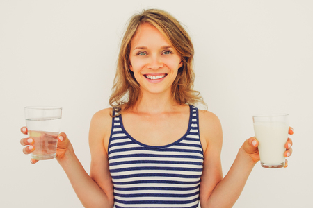 Smiling Lady Holding Glasses of Water and Milkの写真素材