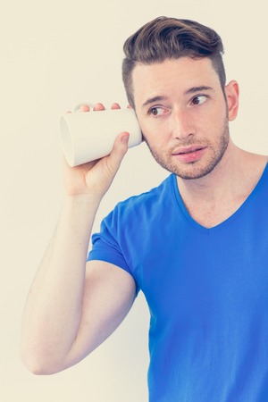 Concentrated young man eavesdropping with mug