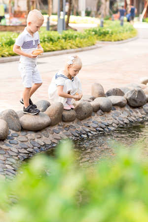 Brother and Sister Feeding Fish in City Pondの写真素材