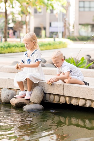 Little Sister and Brother Feeding Fish in Pondの写真素材