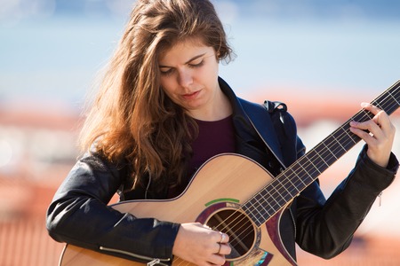 Serious Pretty Girl Playing Acoustic Guitar Outdoorsの写真素材