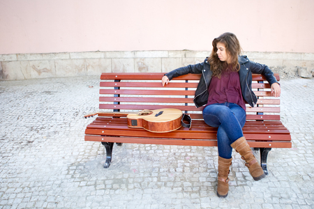 Dreamy Young Woman with Guitar on Bench Outsideの写真素材