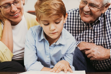 Serious little boy reading book with grandparents