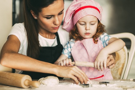 Concentrated girl kneading dough with young motherの写真素材
