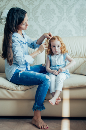 Loving mother braiding hair of her little daughterの写真素材
