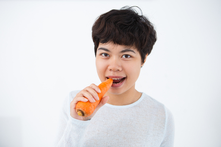 Cheerful Asian woman eating fresh carrotの写真素材