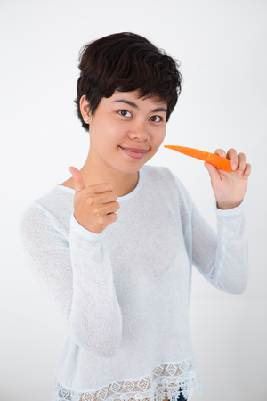 Positive woman eating carrot and showing thumb-upの写真素材
