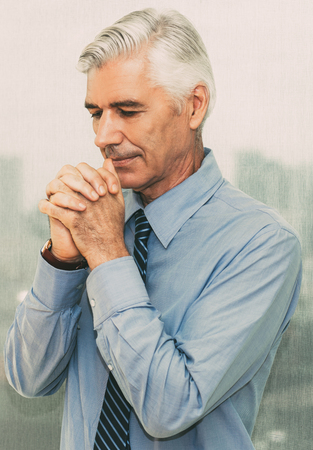 Pensive senior businessman praying in officeの写真素材