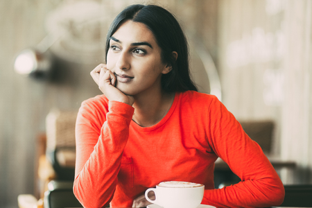 Dreamy Indian girl sitting at table in restaurantの写真素材