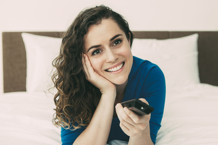 Smiling Beautiful Woman Watching TV on Bedの写真素材