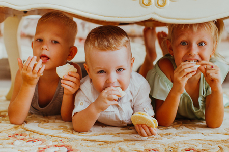 Little Boys and Girl Eating Cookies Under Tableの写真素材