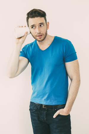 Concentrated young man eavesdropping with mugの写真素材