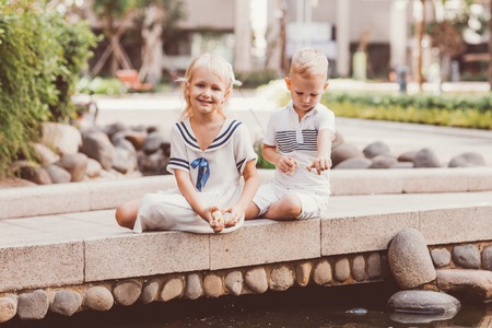 Smiling Girl and Boy Feeding Fish in City Pondの写真素材