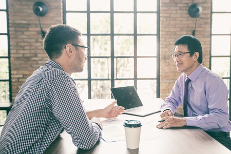 Closeup of two smiling business men discussing issues and working at cafe table with brick wall and...