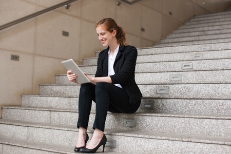 Portrait of happy young Caucasian businesswoman or student wearing costume sitting on stairs and...