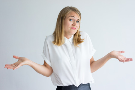 Portrait of confused young Caucasian businesswoman wearing white shirt shrugging shoulders....