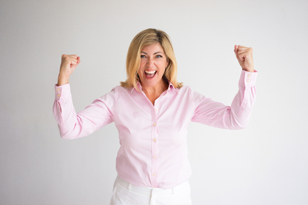 Closeup portrait of cheerful middle-aged attractive fair-haired woman looking at camera, pumping fists and celebrating success. Success concept. Isolated front view on grey background.の写真素材