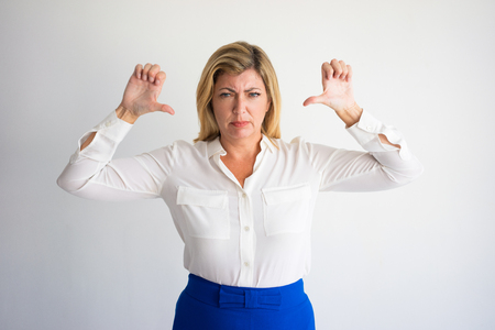 Angry mature Caucasian woman in formal blouse showing thumbs down. Annoyed boss dissatisfied with employees work. Business failure and displeasure concept.の写真素材