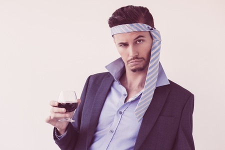 Closeup of drunk business man looking at camera, wearing tie on his head and holding glass of wine. Isolated view on white background.の写真素材