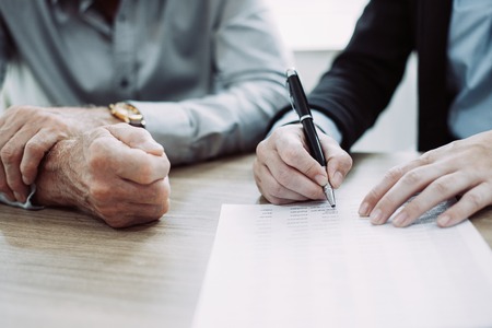 Unrecognizable woman signing contract at meeting, businessman sitting near her and controlling process of deal. Or female hands analyzing or examining document. Paperwork or partnership conceptの写真素材