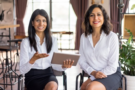Portrait of cheerful multiethnic female colleagues meeting in lounge room. Young Caucasian and Latin American businesswomen working with digital tablet. Women in business and collaboration conceptの写真素材