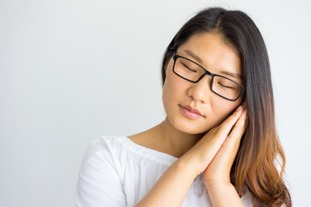 Exhausted attractive young Asian woman sleeping. Serene pretty girl with closed eyes in glasses leaning head on chin. Fatigue conceptの写真素材