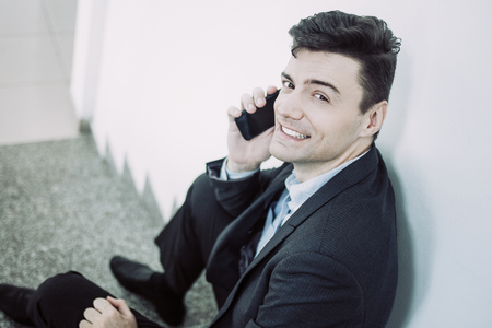 Happy businessman talking on smartphone and sitting on stairs. Young manager calling business partner. Business conceptの写真素材