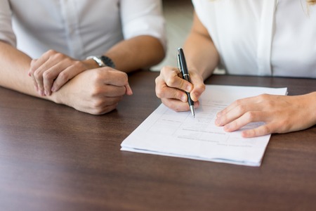 Close-up of female hands filling in questionnaire at job interview. Young Caucasian businesswoman sitting at table with male partner and signing contract. Job interview and signing contract conceptの写真素材