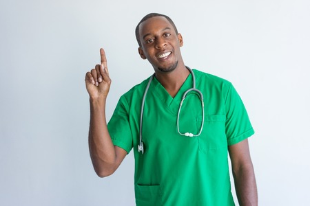 Portrait of happy young African American doctor having idea. African American general practitioner wearing green medical garment showing forefinger and smiling at camera. Having idea conceptの写真素材