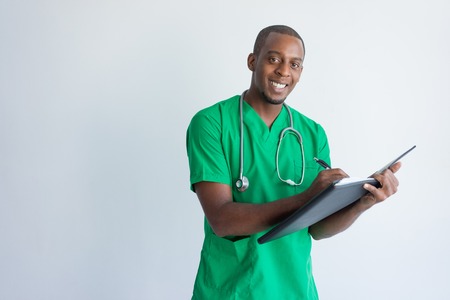 Positive young general practitioner filling in medical record. Portrait of African American medic wearing green medical garment holding folder and smiling at camera. Diagnosis conceptの写真素材