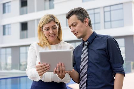 Content business people reading news on tablet computer outdoors. Businesspeople standing with building in background. Technology in business concept.の写真素材