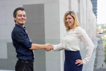 Happy male and female business partners shaking hands outdoors. Businesspeople looking at camera and...