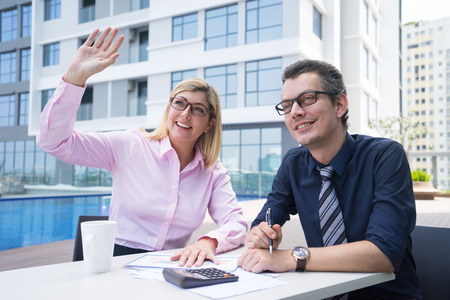 Happy attractive businesswoman waving hand while sitting at table with colleague in outdoor cafe.の写真素材