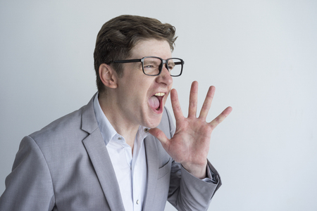 Angry emotional businessman screaming aside and holding hand near mouth. Aggressive emotionally disturbed boss shouting. Emotional stress conceptの写真素材