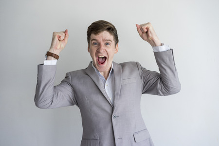 Cheerful hilarious young male entrepreneur celebrating success. Excited handsome businessman in gray formalwear making yes sign and screaming at camera. Expression conceptの写真素材