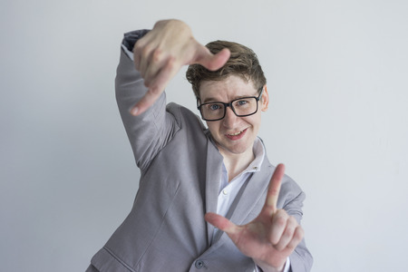 Cheerful positive creative male manager making frame gesture and looking at camera. Jolly handsome young businessman in eyeglasses gazing at camera. Planning conceptの写真素材