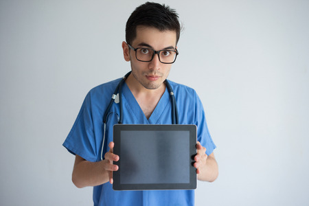 Serious young male doctor showing tablet computer screen. Technologies in medicine concept. Isolated front view on white background.の写真素材