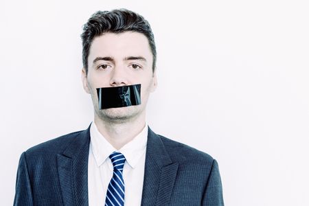 Portrait of young Caucasian businessman wearing suit looking on camera with adhesive tape on mouth. Censorship conceptの写真素材