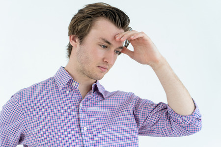 Pensive young man touching forehead and thinking hardの写真素材