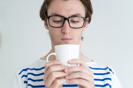 Concentrated thoughtful man in glasses looking at bottom of mug. Serious young man reflecting while drinking tea. Deep in thoughts conceptの写真素材