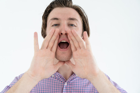 Emotional fan screaming at camera and holding hands near mouth to make sound louder. Handsome young man shouting while calling. Yelling conceptの写真素材