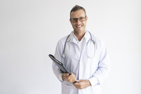 Portrait of happy mid adult doctor wearing glasses with folder. Caucasian general physician wearing lab coat and stethoscope looking at camera and smiling. Medical staff conceptの写真素材