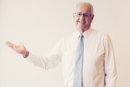 Portrait of senior Caucasian businessman wearing eyeglasses standing in studio and advertising something showing it with handの写真素材