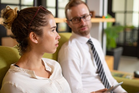 Pensive woman talking with coworker in office lobby. Business man and woman sitting on couch. Business colleagues concept.の写真素材