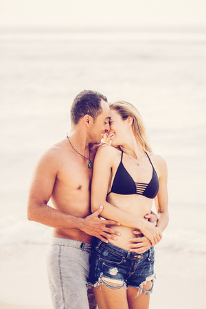 Portrait of happy young Caucasian couple embracing and kissing on beach on summer vacationの写真素材