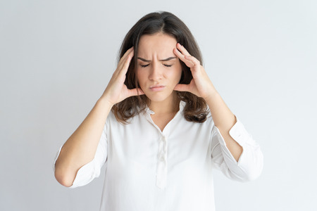Frustrated tired girl suffering from headache. Young Caucasian woman in white blouse touching head with pain grimace. Health care and head ache conceptの写真素材