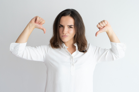 Content girl in white shirt proud of herself. Young Caucasian woman pointing both thumbs at herself. Boasting, vanity, self satisfaction conceptの写真素材