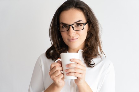 Smiling pretty young woman holding mug and looking at camera. Lady drinking tea or coffee. Break concept. Isolated front view on white background.の写真素材