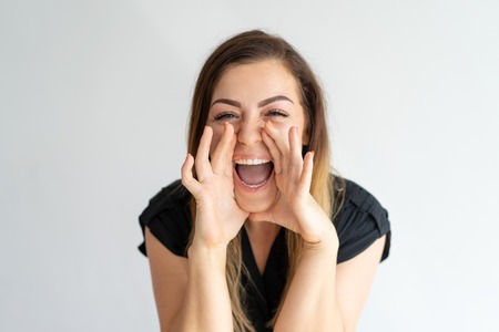 Happy excited lady screaming loud, sharing great news. Cheerful young Caucasian woman with hands at face shouting of joy. Good news conceptの写真素材