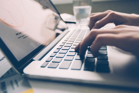 Close-up of hands of businesswoman sitting at table and typing on laptop in officeの写真素材